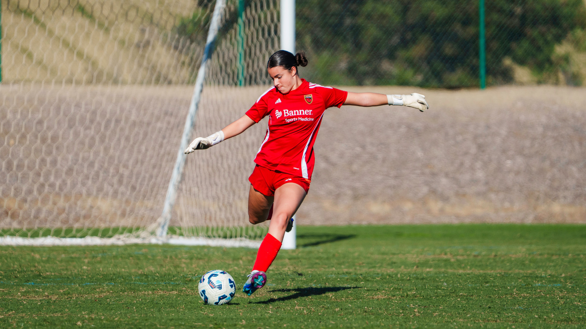 Female youth soccer goalkeeper kicking ball